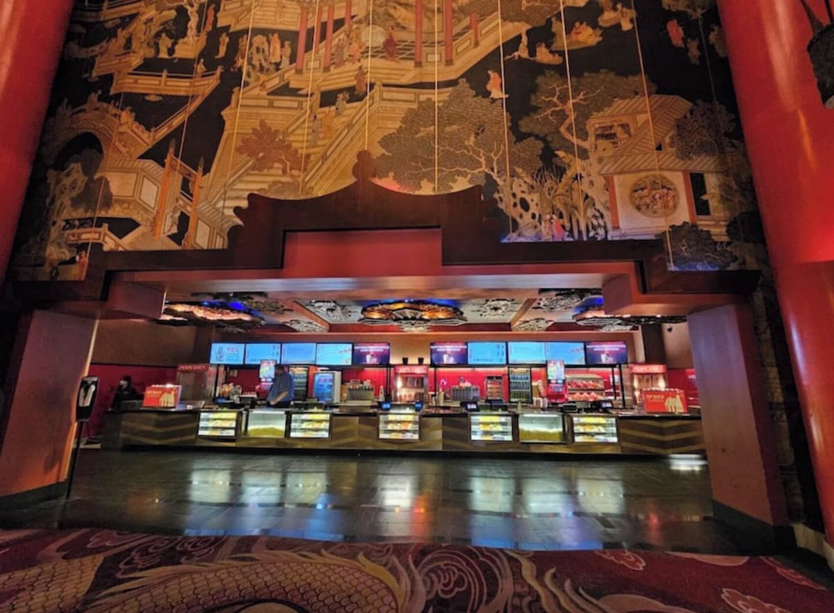 A lobby with a traditional Asian architectural design, featuring intricate wall murals and a modern reception area with digital displays.