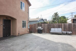 A residential area with a concrete driveway, a wooden fence, a barbecue grill, and a grey sofa. - Cozy and Spacious 5 bedrooms House at Duplex (Vernon)