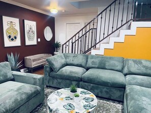 A living room with a green sofa set, a coffee table with a floral pattern, and a staircase with a yellow wall.