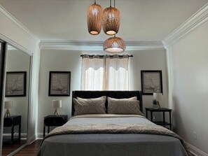 A bedroom with a bed, two bedside tables, a mirror, and a hanging light fixture.