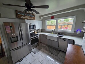 A modern kitchen with stainless steel appliances, a wooden sign above the stove, and a window with a view of the backyard.