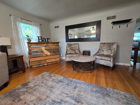 A living room with a wooden bar counter, patterned sofas, a round table, and a large mirror on the wall.