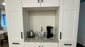 Una cocina blanca con encimera de granito, una tetera, una cafetera y un cubo de basura.