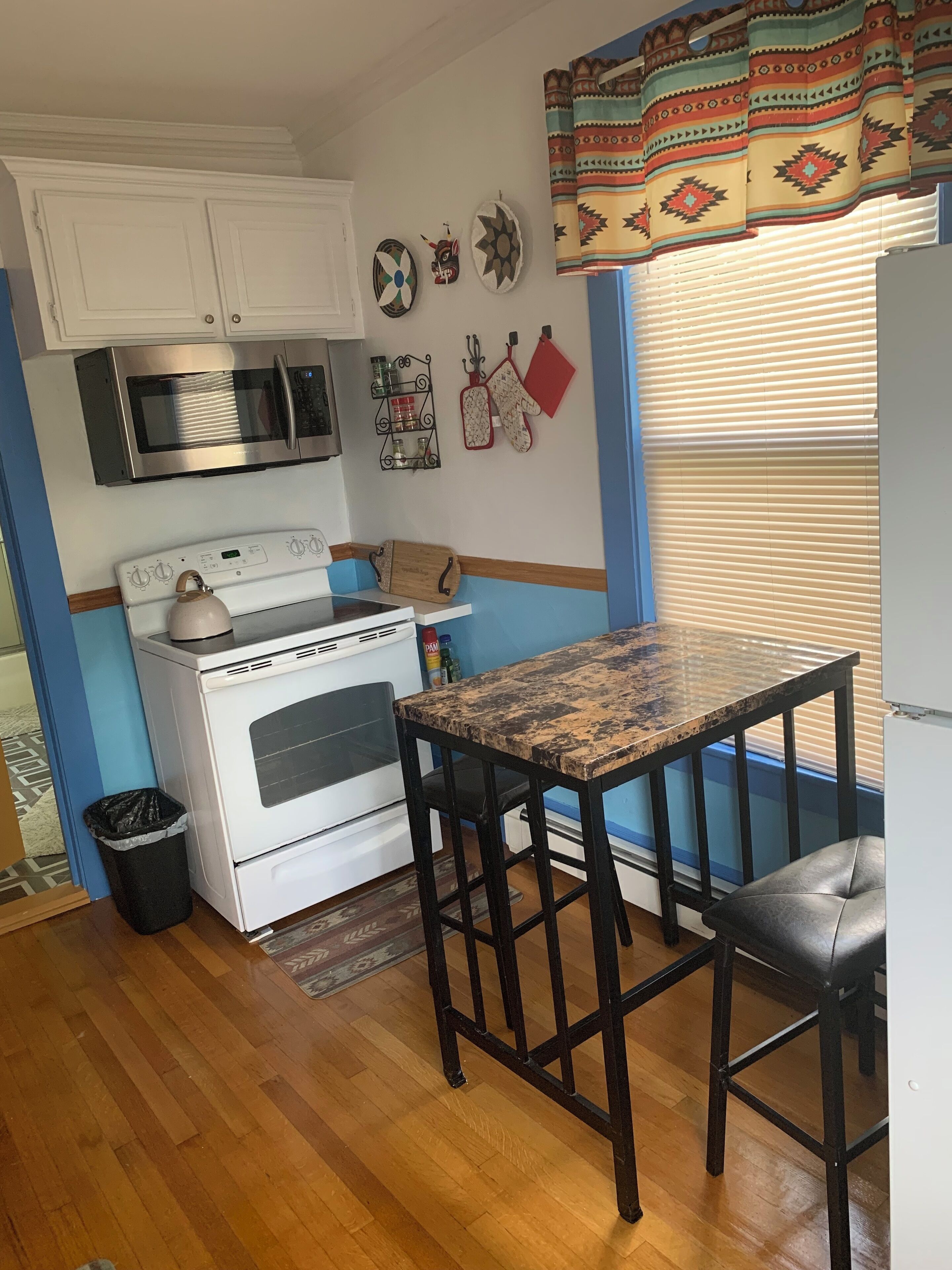 A kitchen with a stove, microwave, and oven. There is a window with blinds and a curtain.