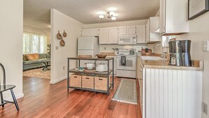 A modern kitchen with white cabinets, a stainless steel refrigerator, a microwave, and a stove. There is a small island with a sink and a coffee maker. - Charming 3-bedroom cottage  (Abingdon)