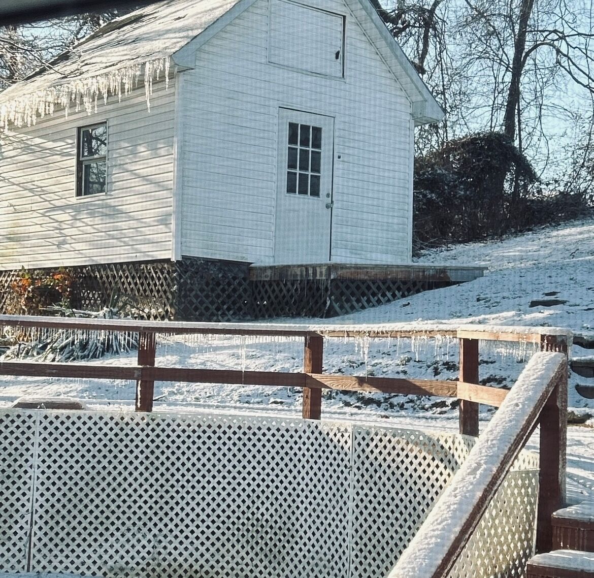 A white wooden building with a small window and a door, surrounded by snow.