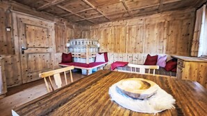 En stuga med träpanel på insidan, med en central sittgrupp, ett träbord och en öppen spis.