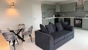 Una cocina moderna con armarios verdes, horno integrado y un comedor con mesa de vidrio y sillas estampadas.