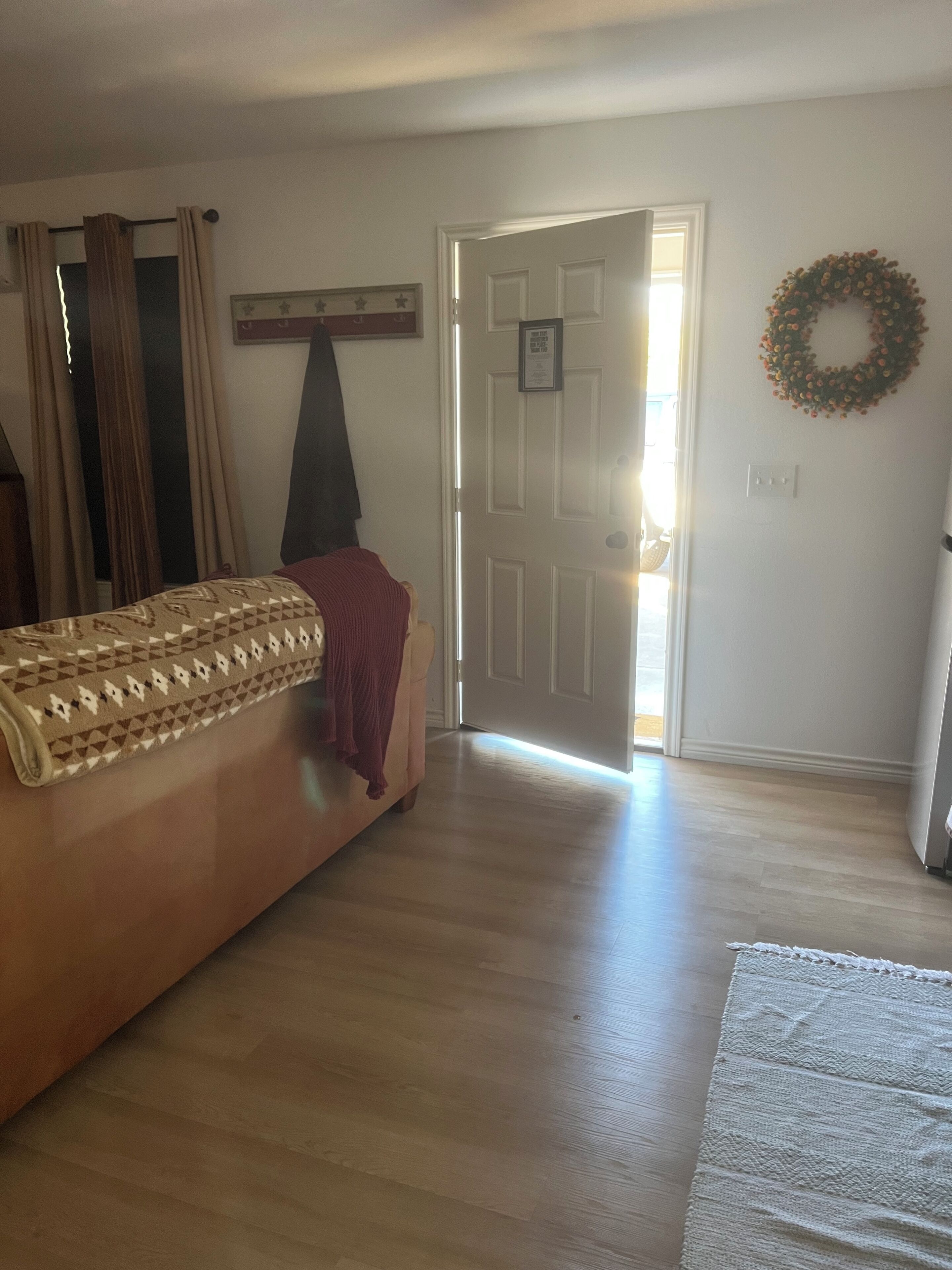 A room with a bed, a door leading outside, a wall-mounted wreath, and a light switch.