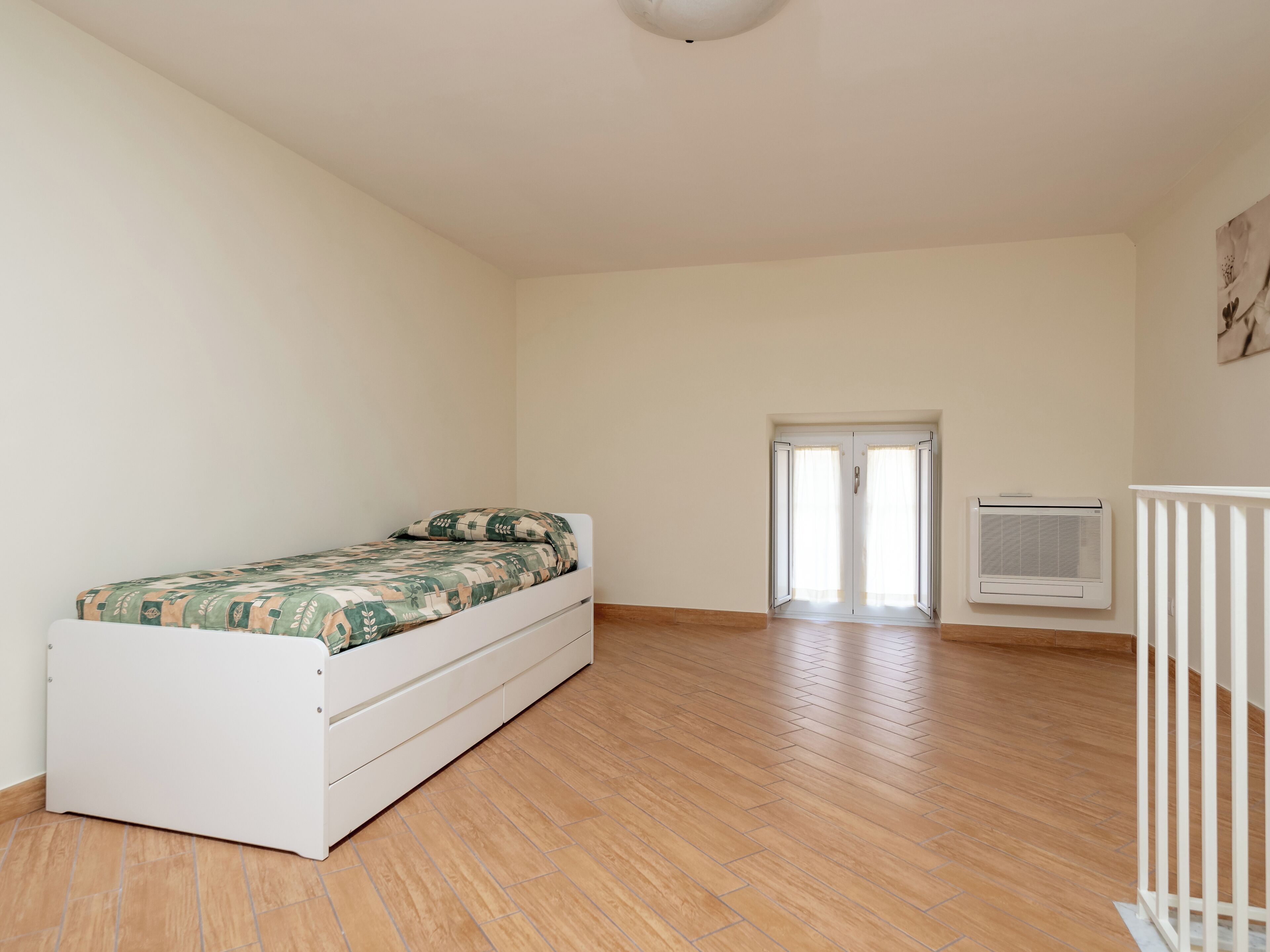 A bedroom with a bed, a white radiator, and a door leading to another room.