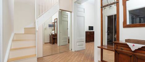 Un pasillo con piso de madera, una escalera, un espejo y un armario de madera.