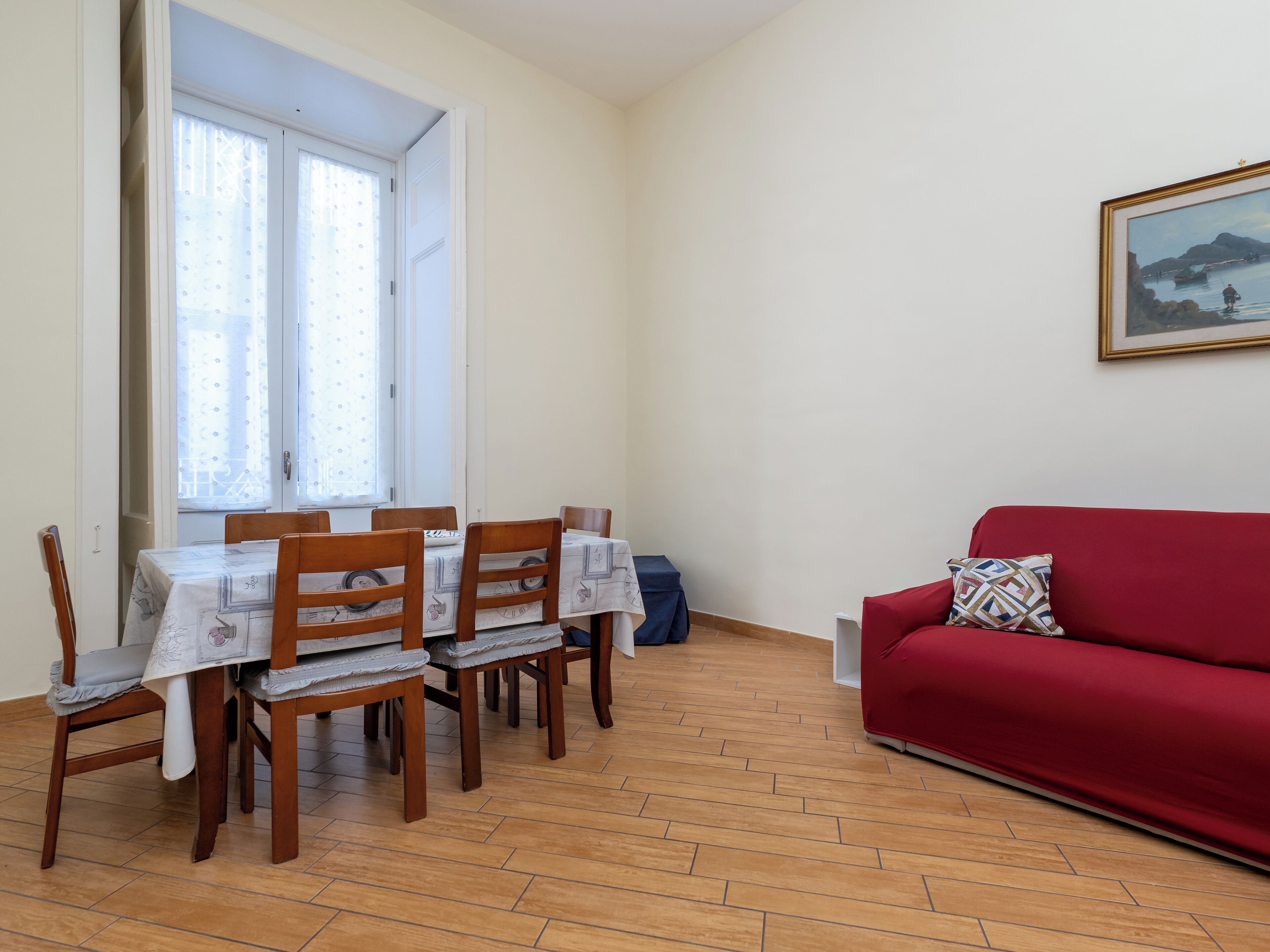 Ein Essbereich mit Tisch und Stühlen, ein rotes Sofa und ein Bild an der Wand.