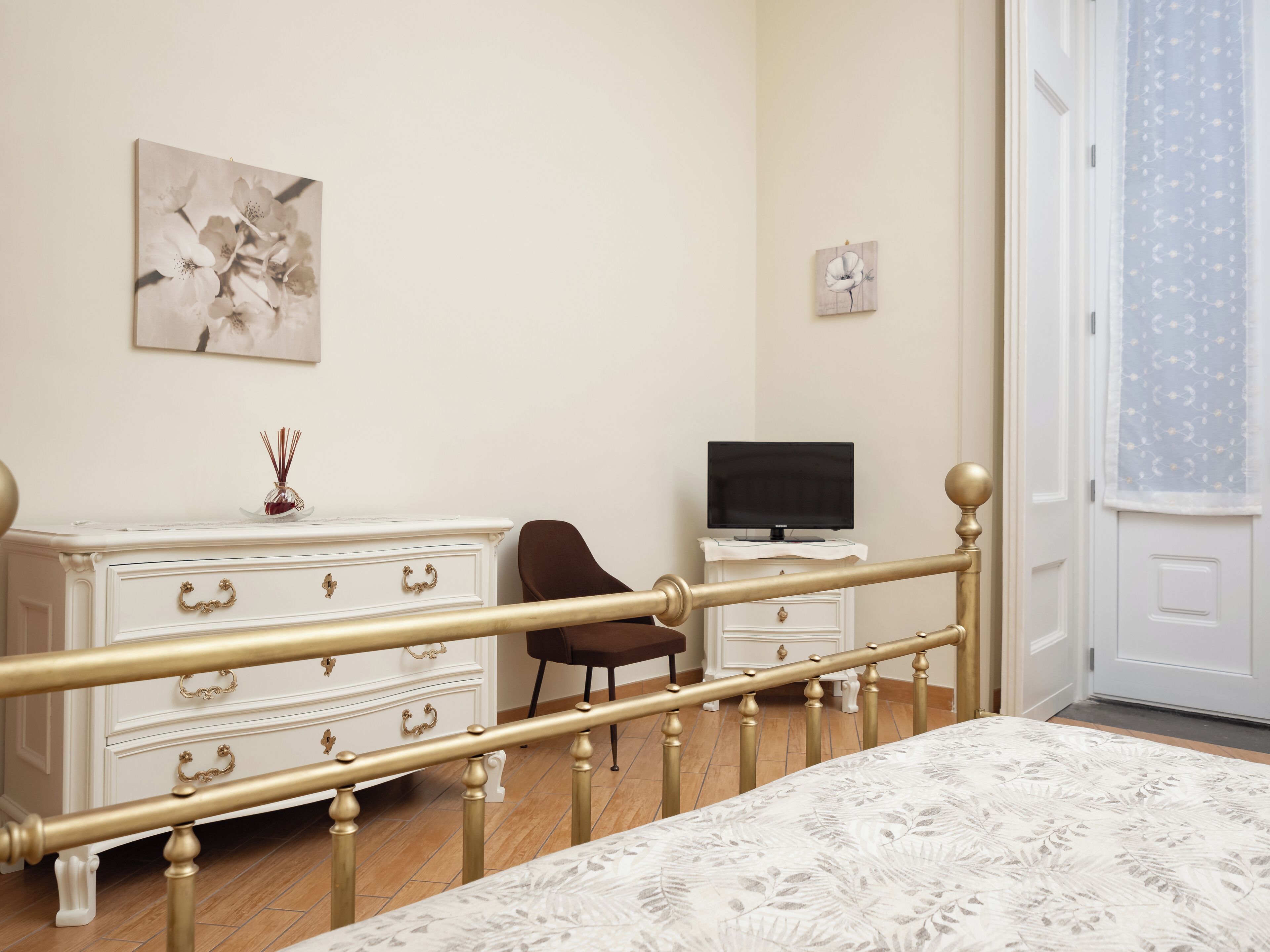 Ein Schlafzimmer mit Bett, Kommode, Sessel, Fernseher und Bildern an den Wänden.