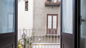 A view from an open door to a balcony with a metal railing, a window with brown shutters, and a small balcony with a white balustrade. - Maya Home (Sorrento)