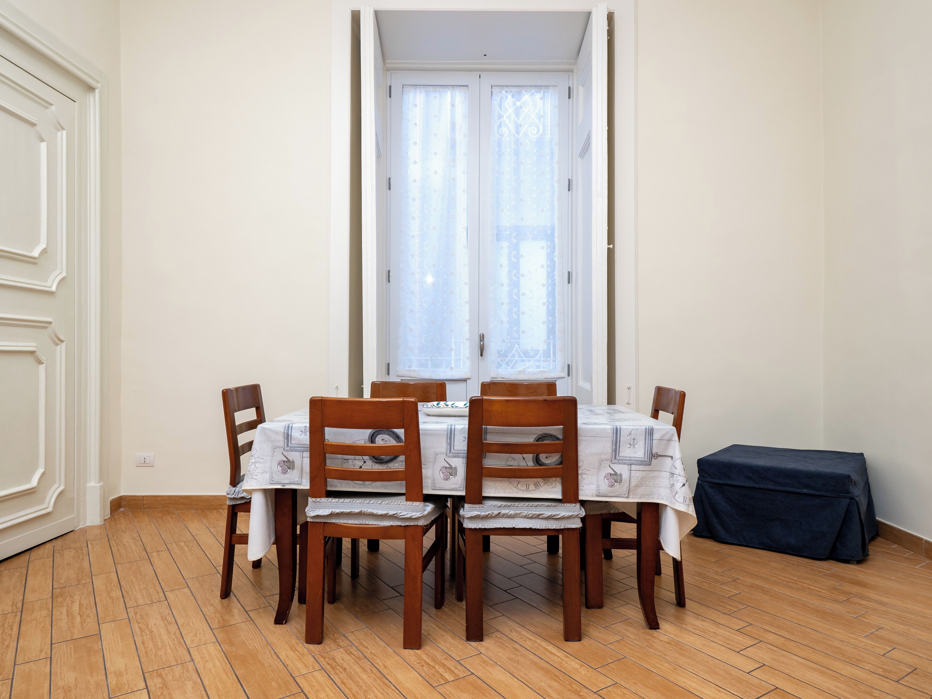 Ein Essbereich mit Tisch und Stühlen, einem Fenster mit Vorhängen und einem Fliesenboden.