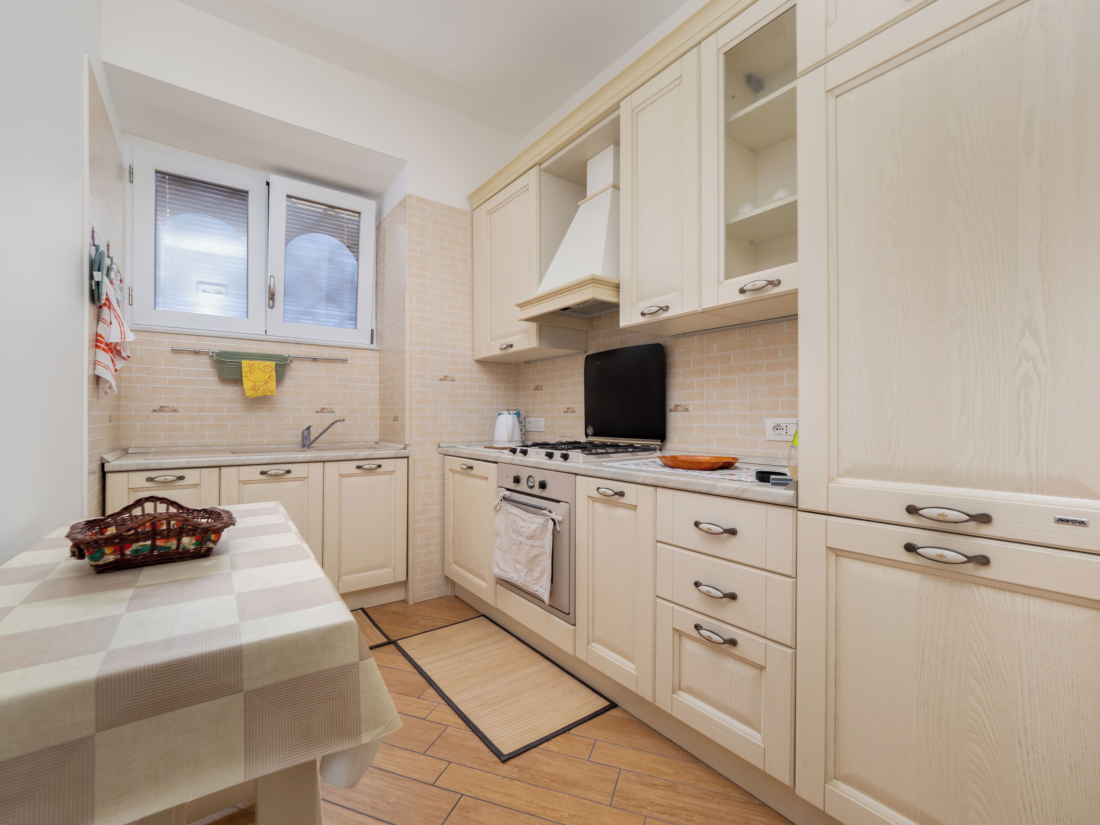 A compact kitchen with a stove, oven, and sink, featuring light-colored cabinets and a checkered tablecloth.