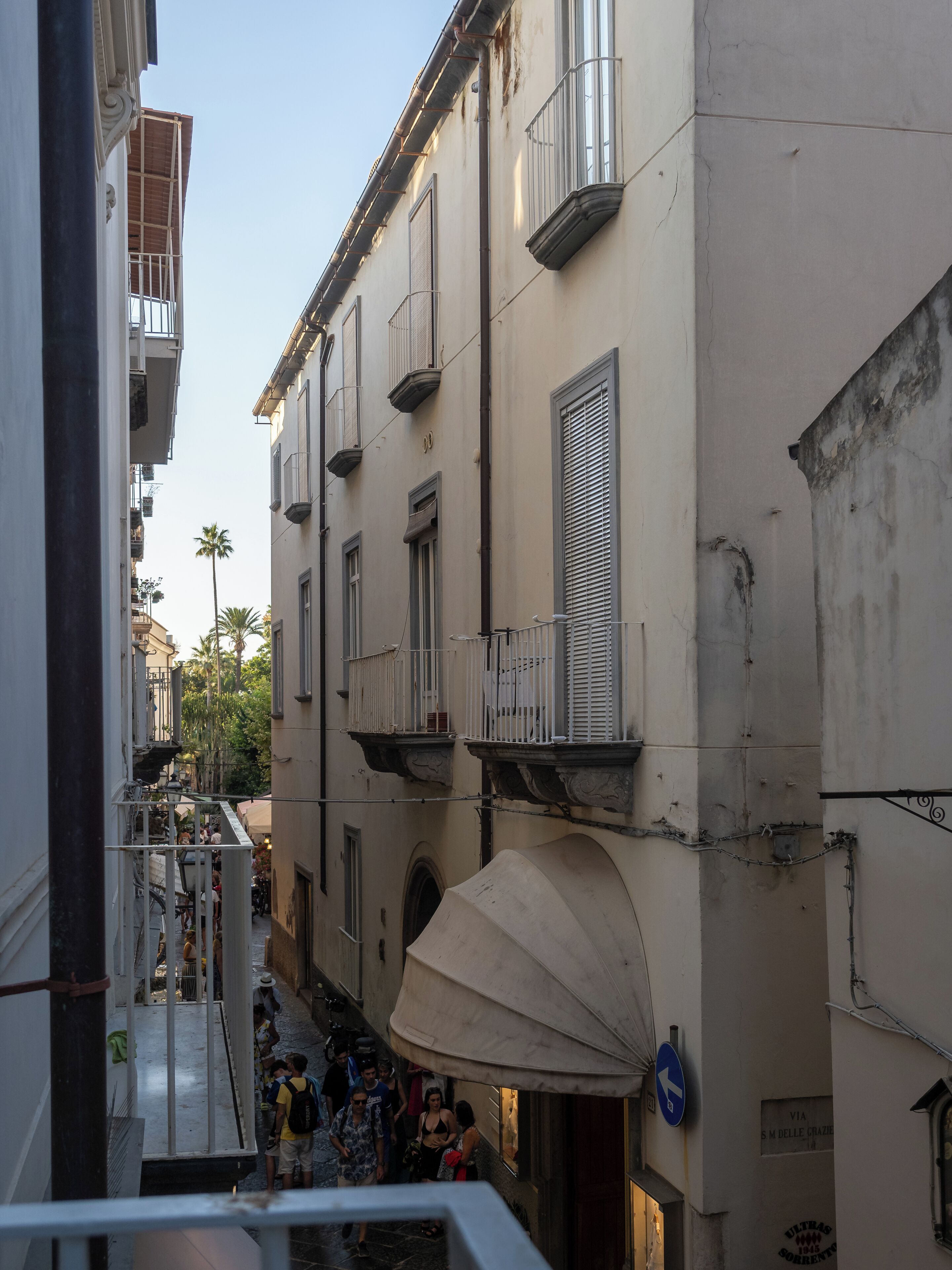 A narrow street with buildings on either side, featuring balconies and a pedestrian walkway.