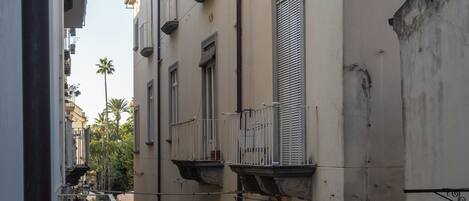 A narrow street with buildings on either side, featuring balconies and a pedestrian walkway.