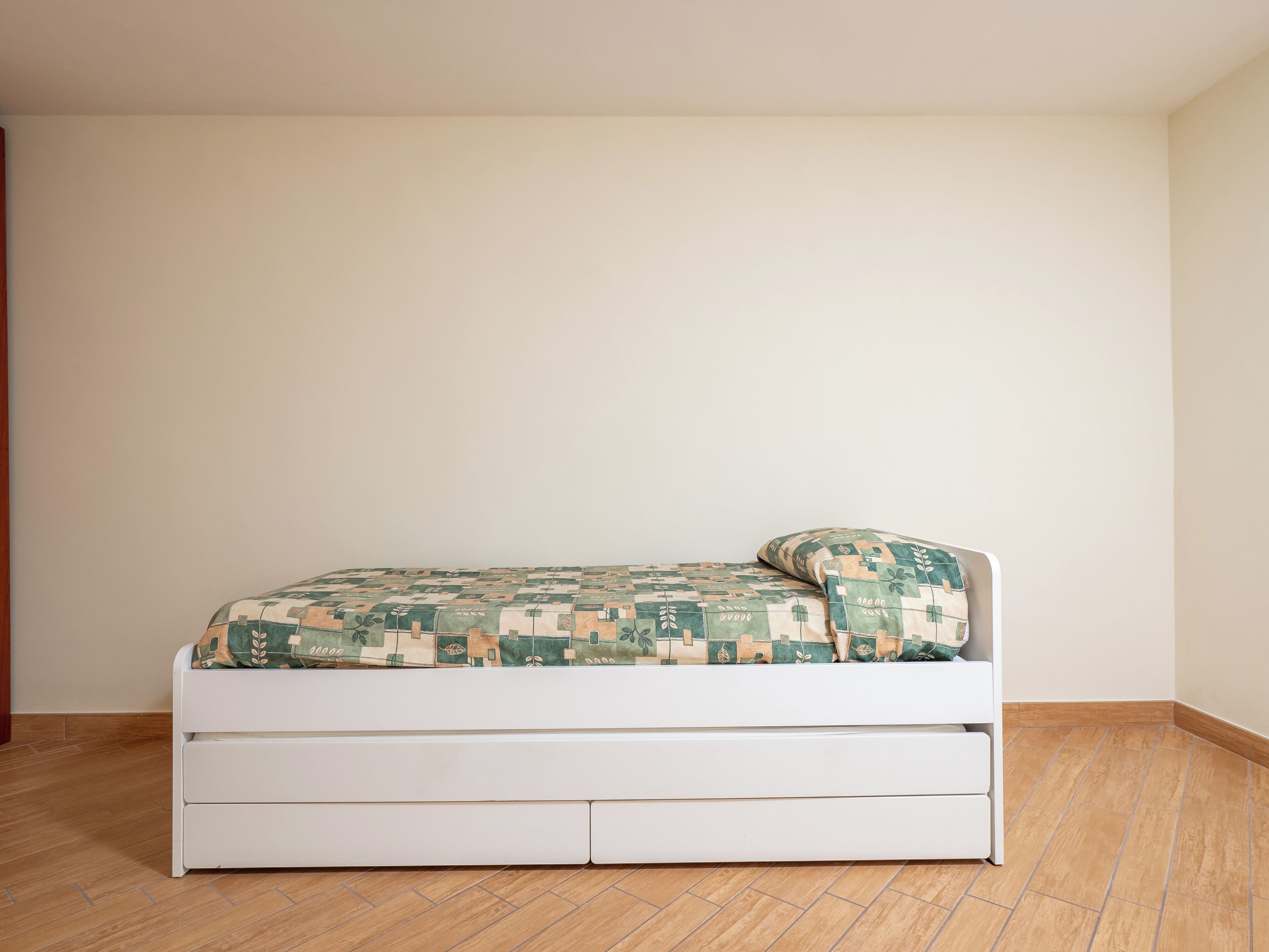 Habitación individual con una cama blanca, una colcha estampada y una pared blanca.