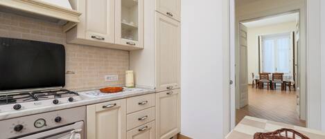 Cocina con estufa, horno y armarios. Hay una mesa de comedor con sillas y una cesta.