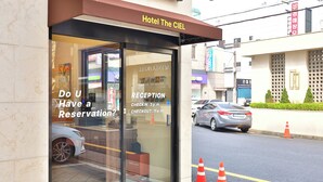 A hotel entrance with a reception desk, a car parked outside, and traffic cones on the sidewalk. - The Ciel Hotel (Gyeongju)