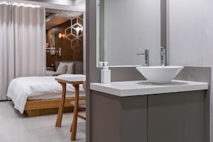 Un baño moderno con un lavamanos blanco, un espejo y una mesita de noche de madera.