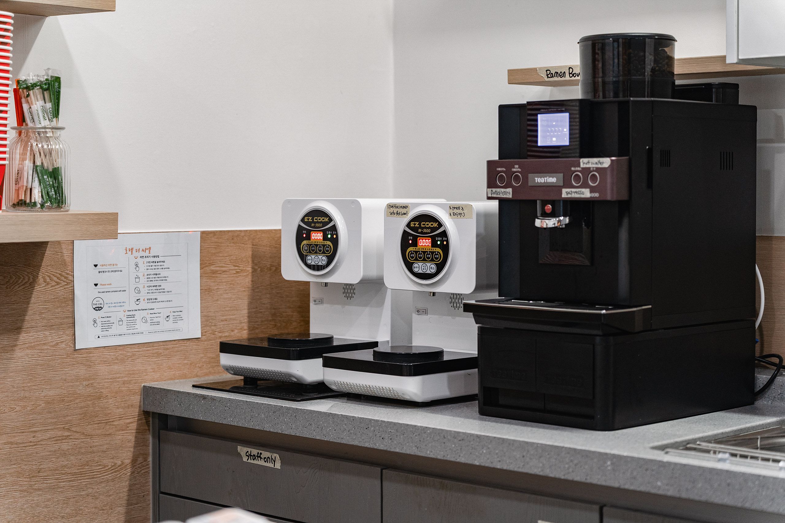 Una máquina de café con dos dispensadores y un panel de control, ubicada sobre un mostrador con un letrero y un menú.