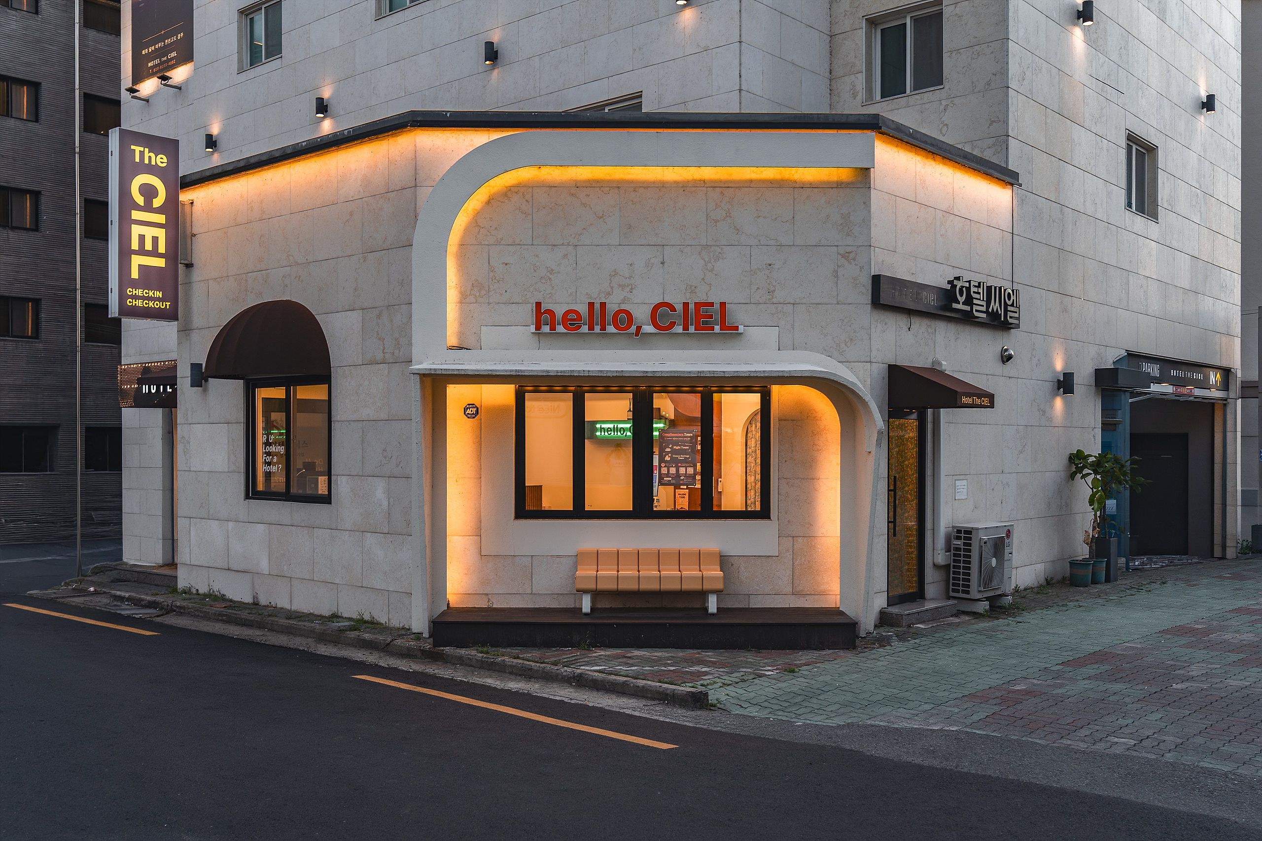 A hotel named 'Hotel The Ciel' with a modern facade, illuminated signage, and a bench outside.