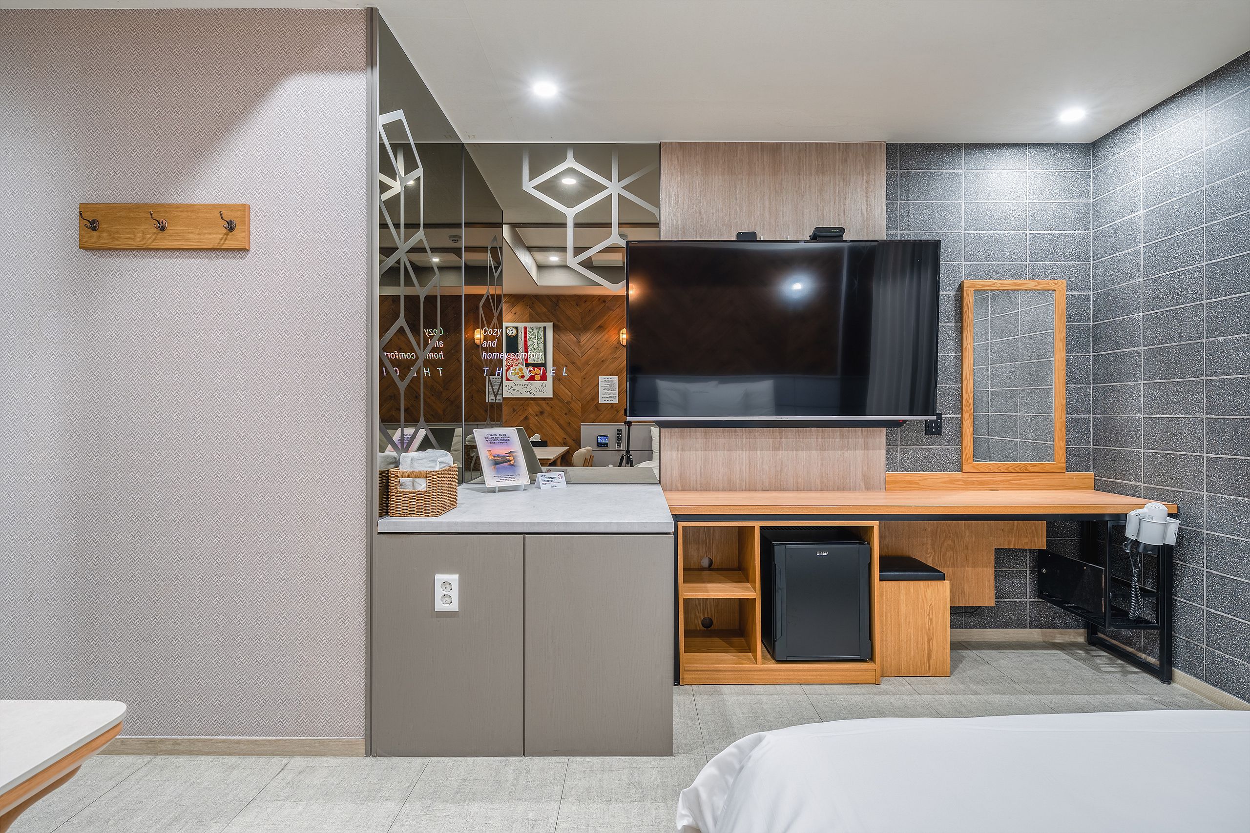 A modern hotel room with a large flat-screen TV, wooden furniture, and a tiled wall.