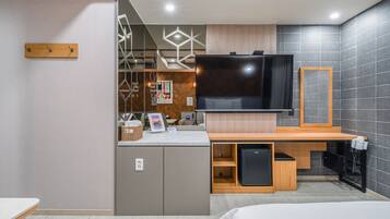 A modern hotel room with a large flat-screen TV, wooden furniture, and a tiled wall.