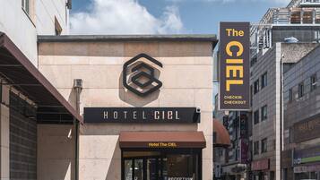 A hotel entrance with a sign reading 'Hotel The Ciel' and a 'Checkin Checkout' sign.