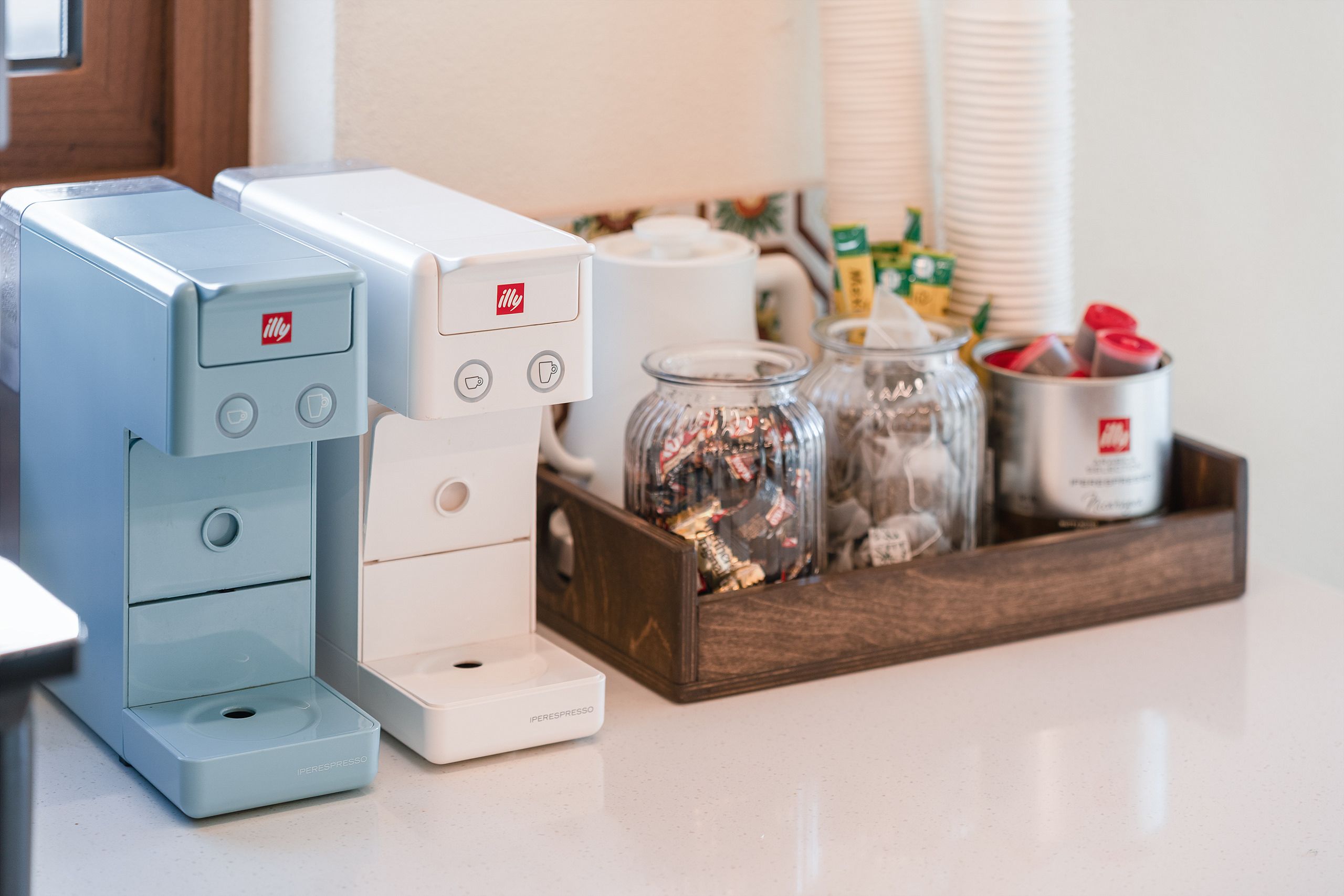 A coffee station with two coffee machines, a tray with jars of coffee beans, and a cup holder.