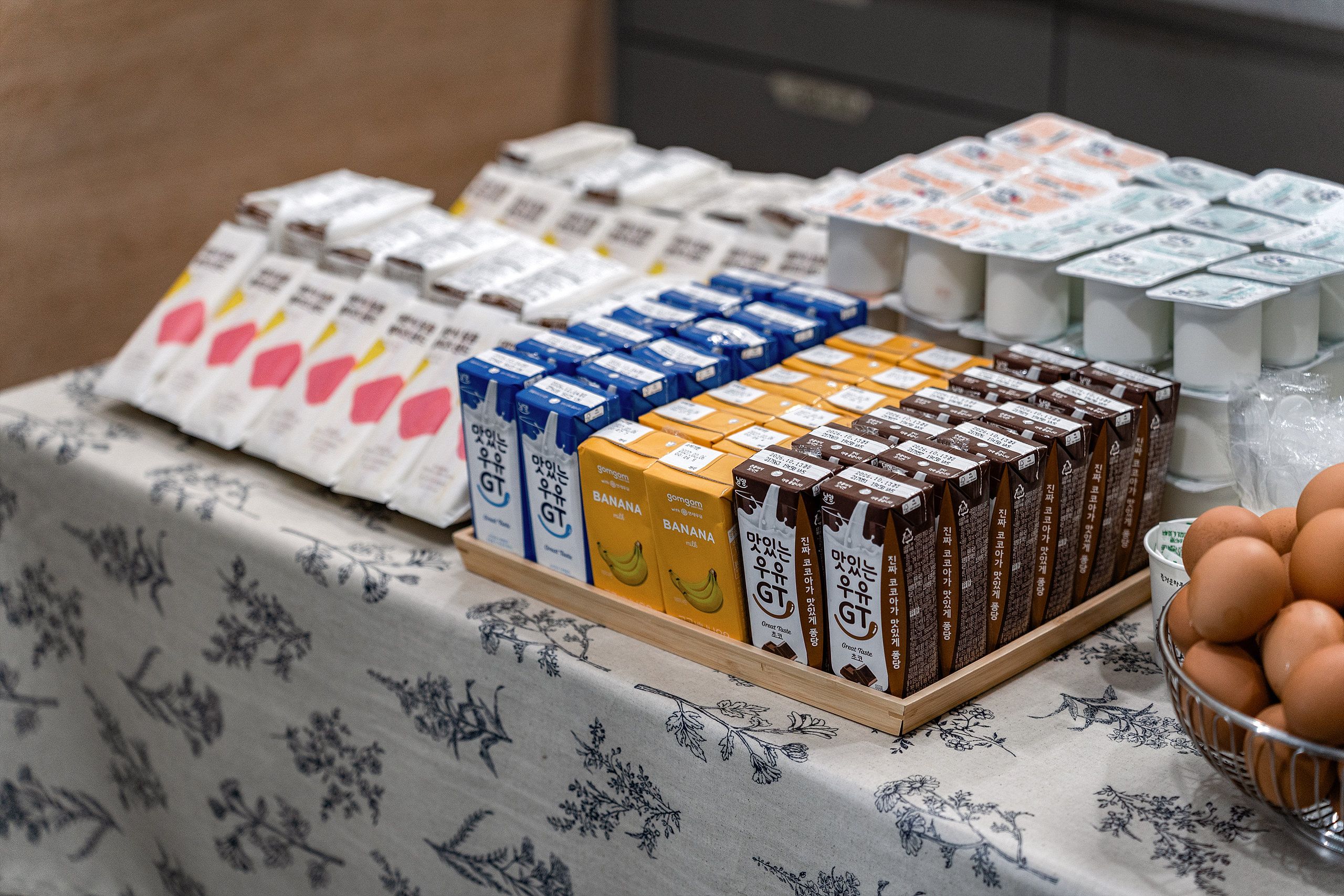 A table with various packaged food items, including boxes labeled with different flavors and a basket of eggs.