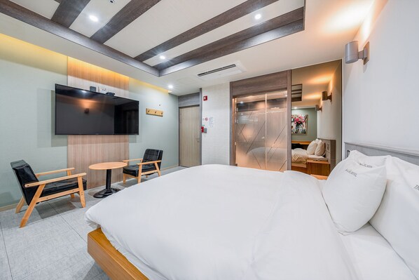 A hotel room with a bed, a desk, a chair, a TV, and a sliding door leading to a bathroom.