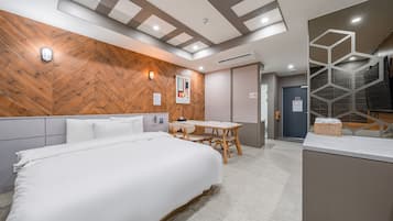 Hotellihuone, jossa on suuri sänky, puukoristeinen seinä, pieni pöytä tuoleineen sekä kylpyhuone, jossa on geometrisesti muotoiltu lasiseinä.