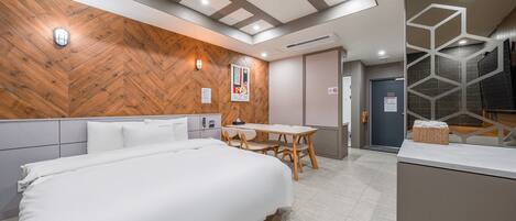Ein Hotelzimmer mit einem großen Bett, einer Wand mit Holzvertäfelung, einem kleinen Tisch mit Stühlen und einem Badezimmer mit einer geometrischen Glasabtrennung.