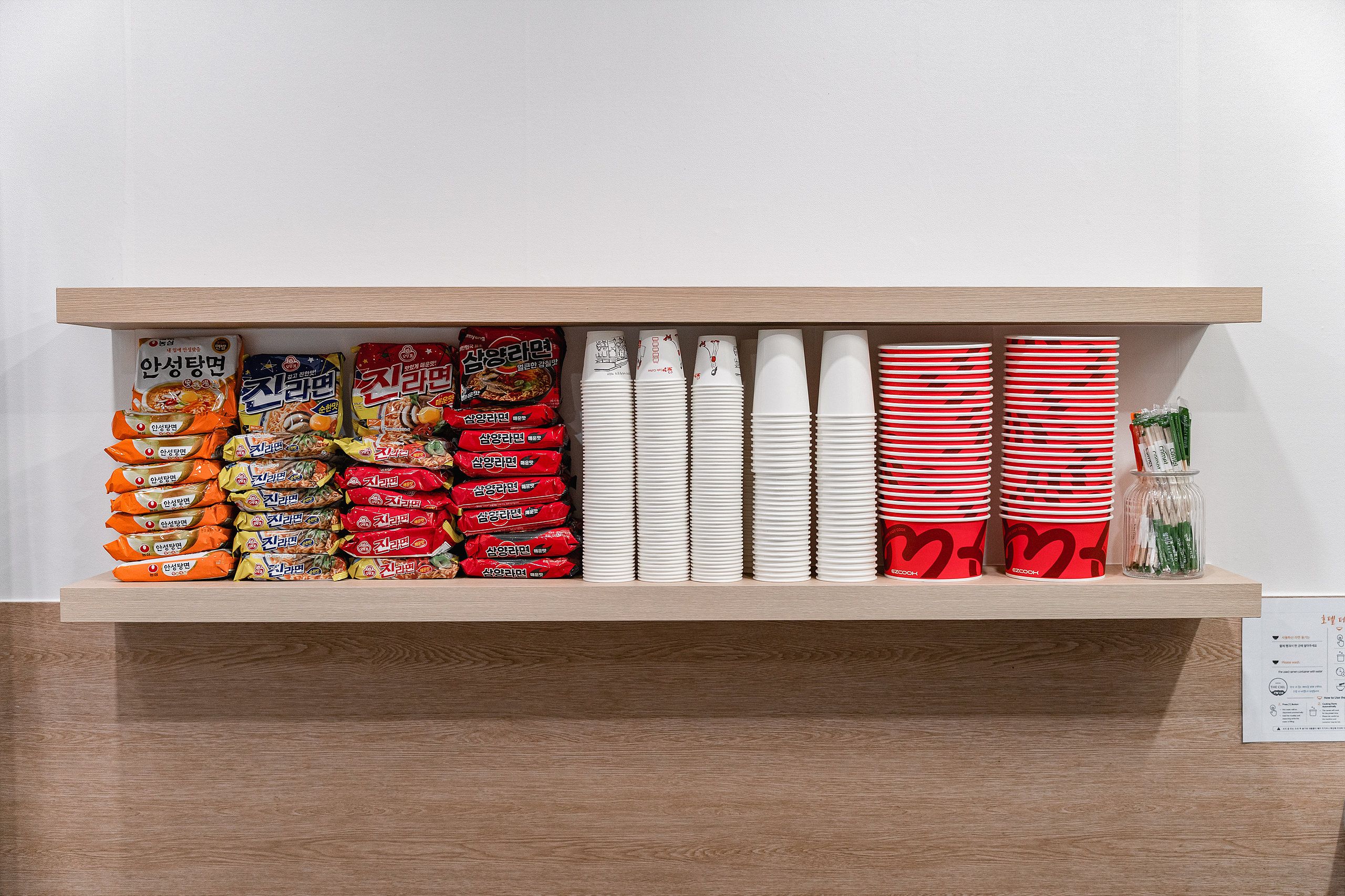 A shelf with various packaged food items and stacked paper cups.