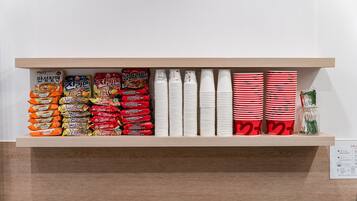 A shelf with various packaged food items and stacked paper cups.