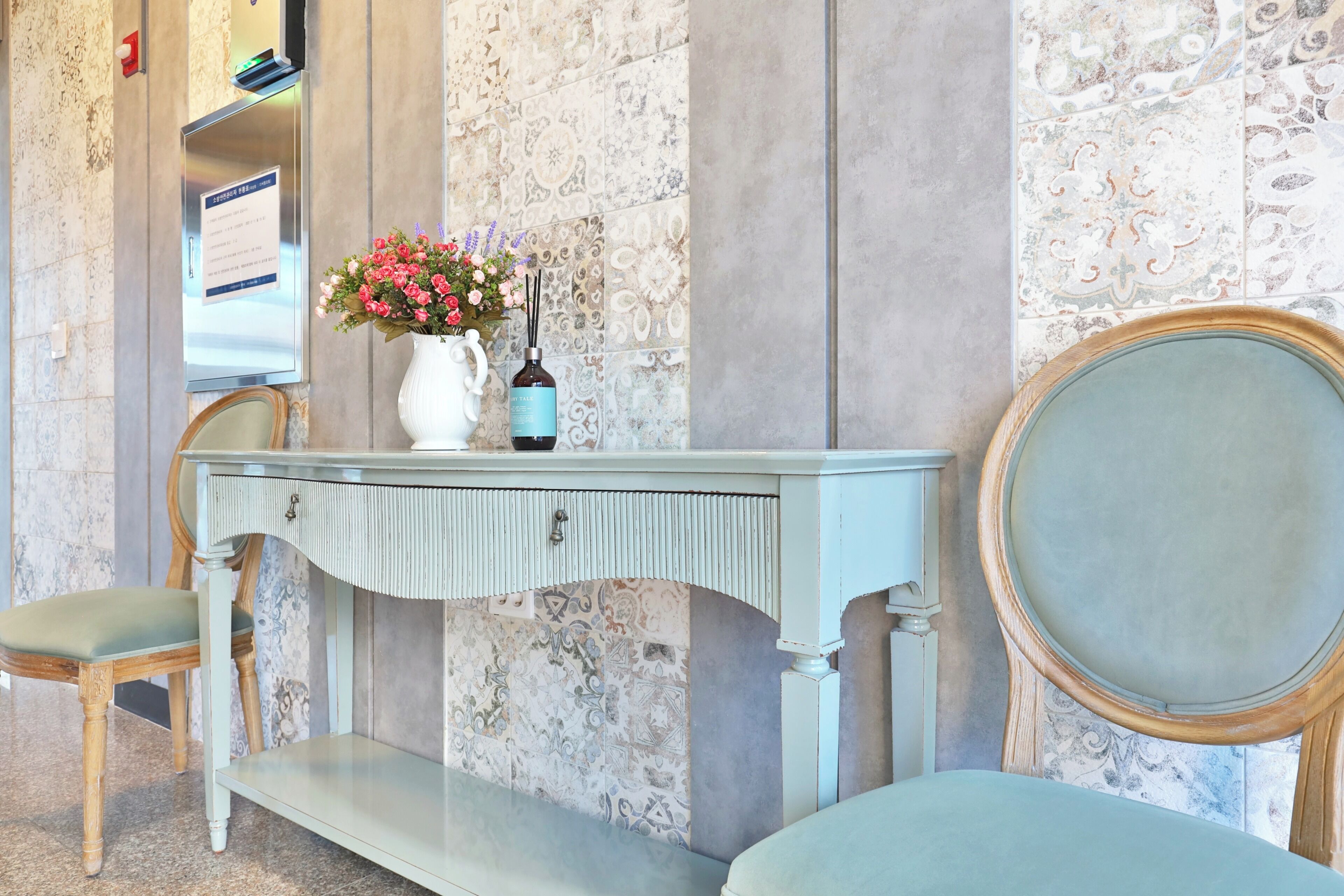 Une pièce avec une console bleu clair, un vase blanc orné de fleurs, un miroir et un banc.