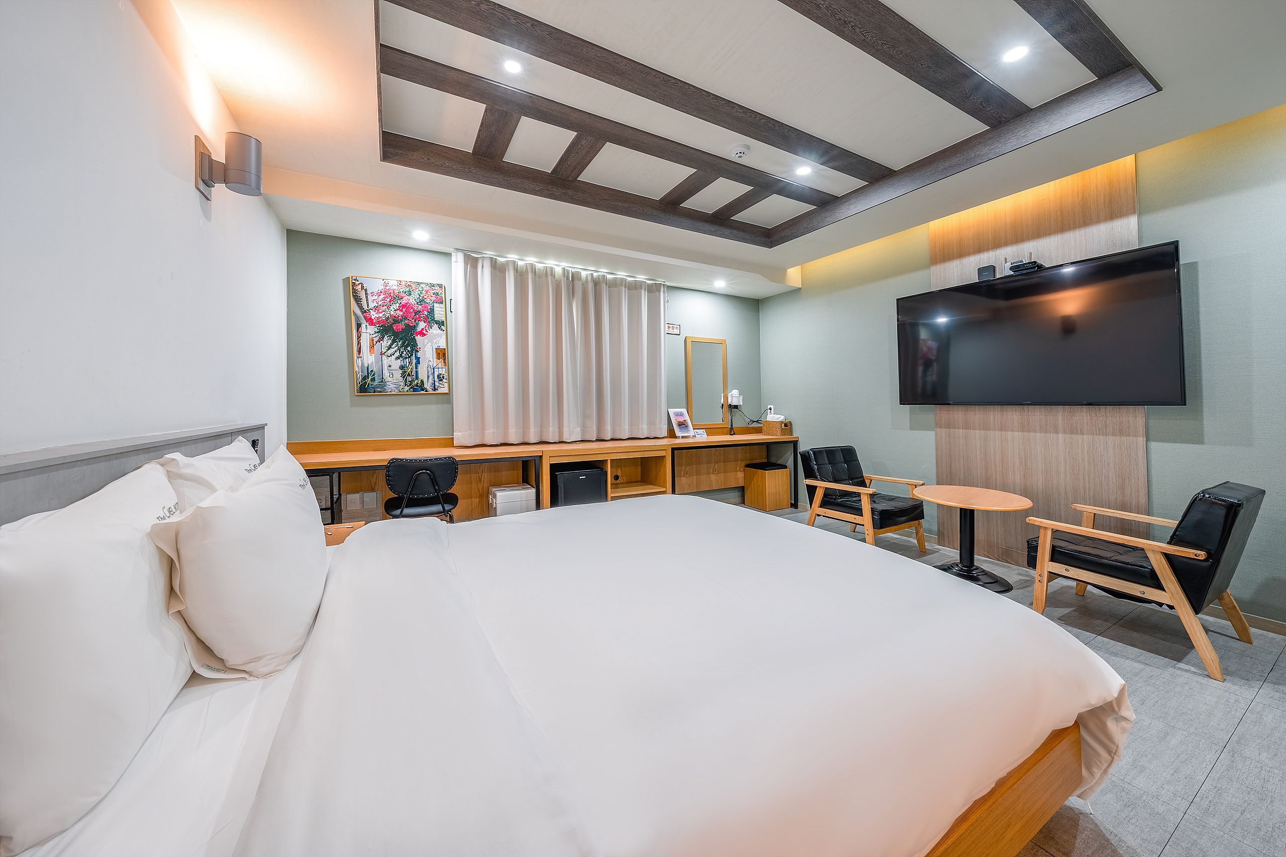 A hotel room with a large bed, a desk with a chair, a television, and a mirror.