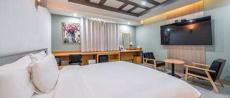 A hotel room with a large bed, a desk with a chair, a television, and a mirror.