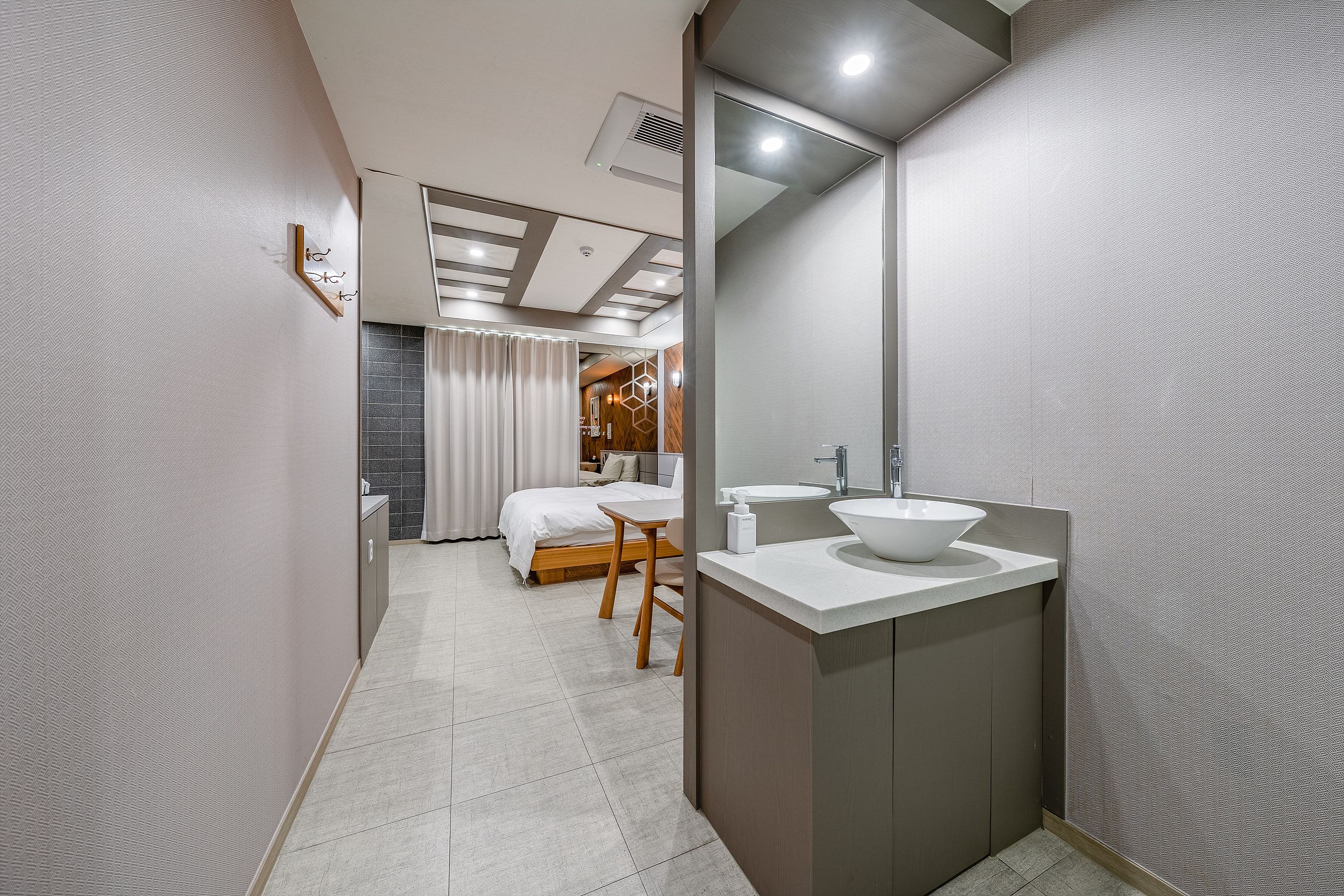 A modern bathroom with a large mirror, a white sink, and a wooden chair.