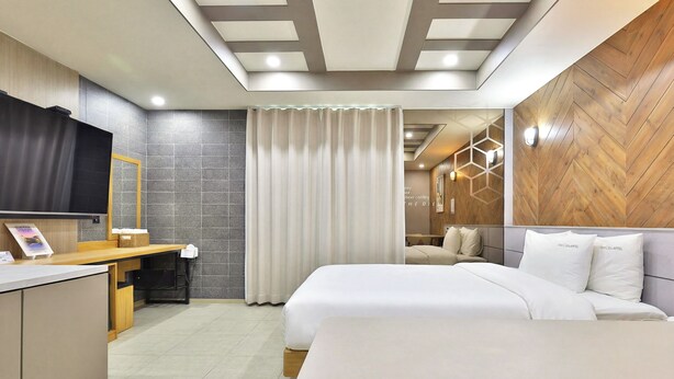 A hotel room with a bed, a desk, a mirror, a TV, and a bathroom with a shower.