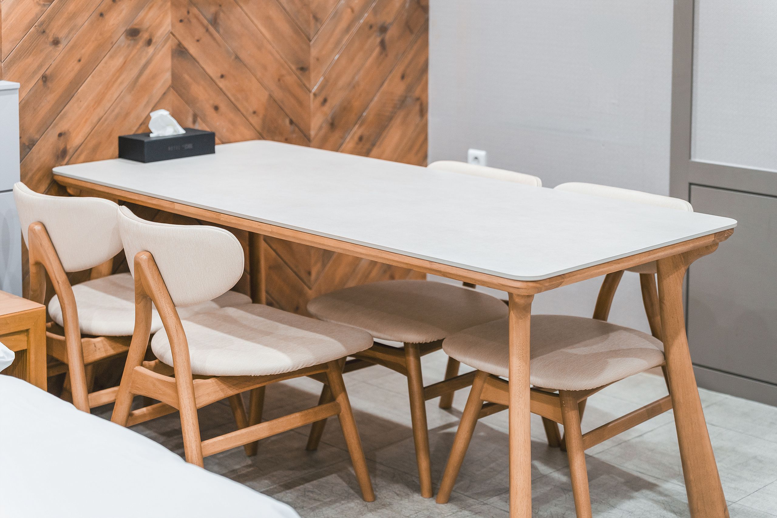 A dining table with four chairs, a tissue box, and a wooden wall in the background.