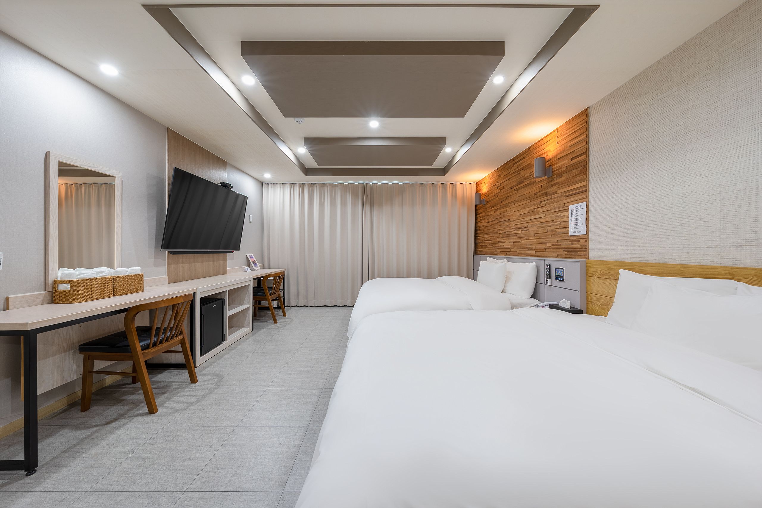 A hotel room with a bed, a desk, a chair, a television, and a wall-mounted light fixture.