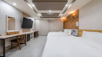 A hotel room with a bed, a desk, a chair, a television, and a wall-mounted light fixture.
