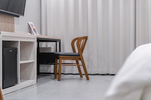 A hotel room with a wooden chair, a desk with a television, and a bed.