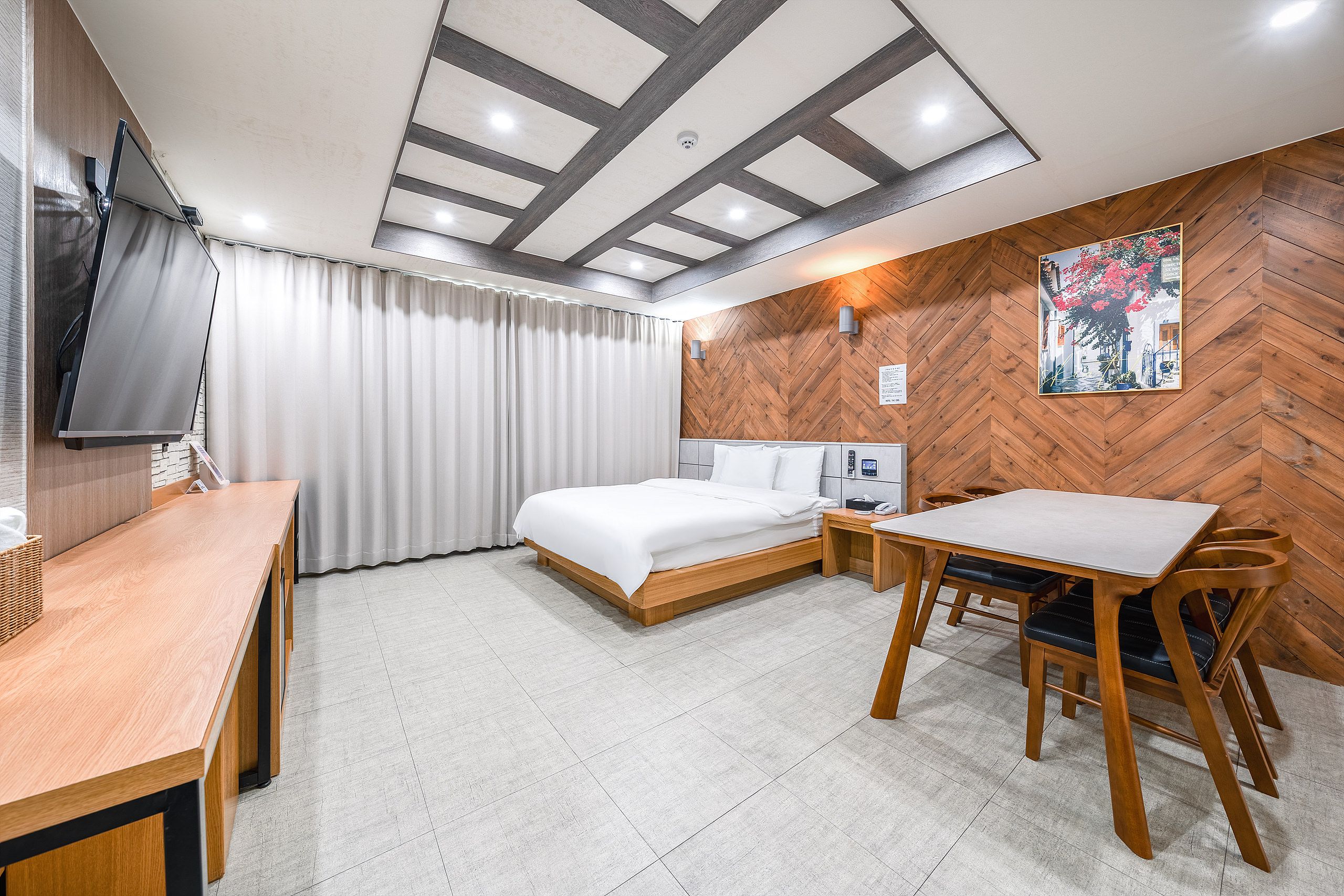 Ein Hotelzimmer mit Bett, Schreibtisch, Stuhl, Fernseher und einer Wand mit Holzverkleidung in Fischgrätmuster.
