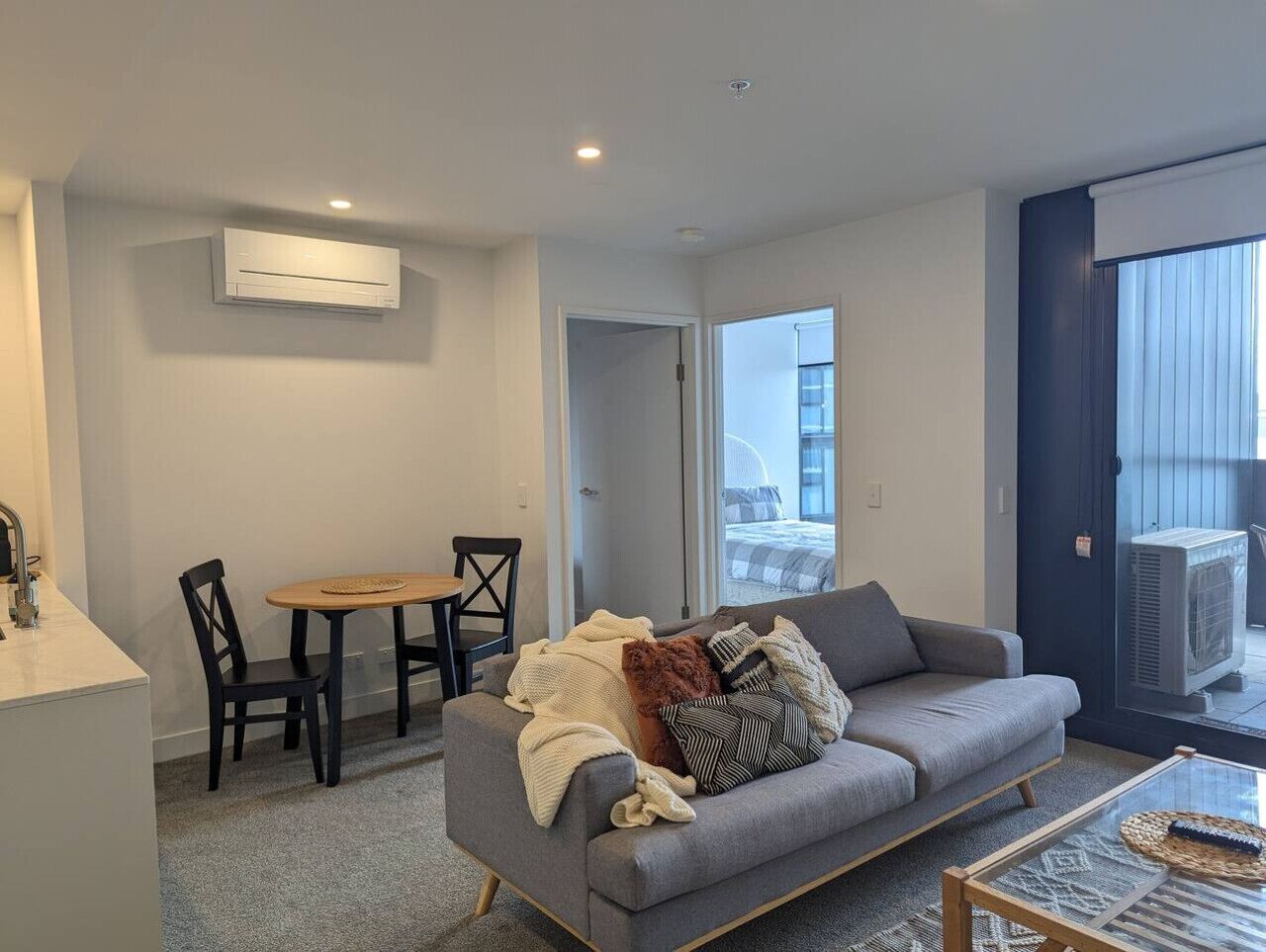 A modern living room with a grey sofa, a wooden coffee table, and a dining area with a table and chairs.