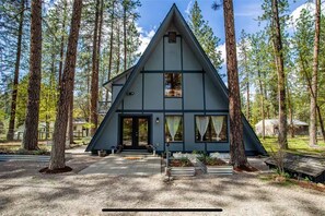Eine dreieckige Hütte mit Veranda, umgeben von hohen Bäumen.